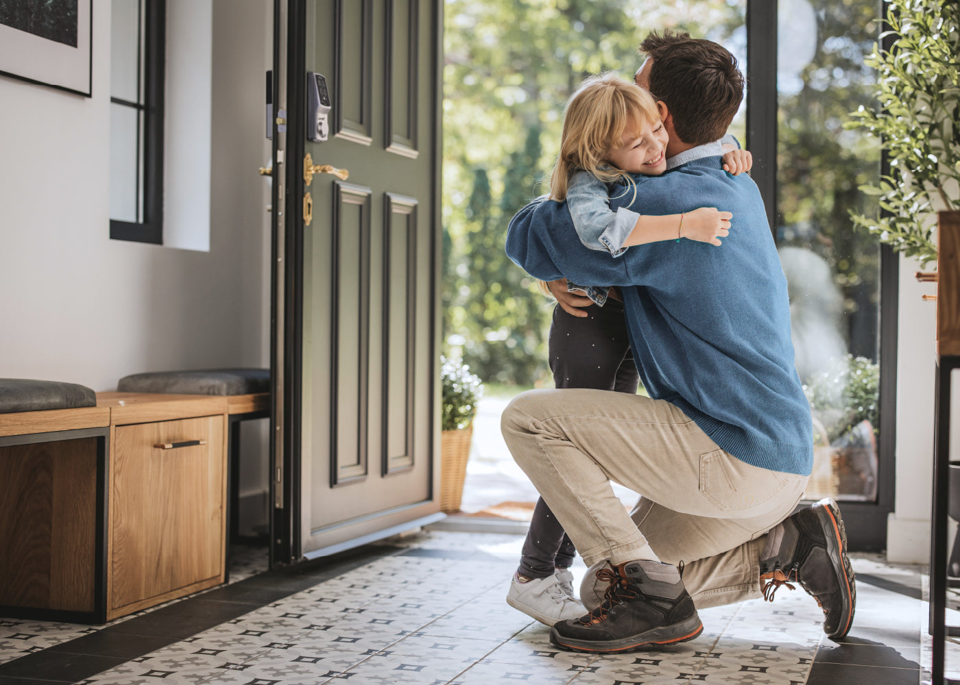 A parent and child hugging on the porch beside a smart lock.